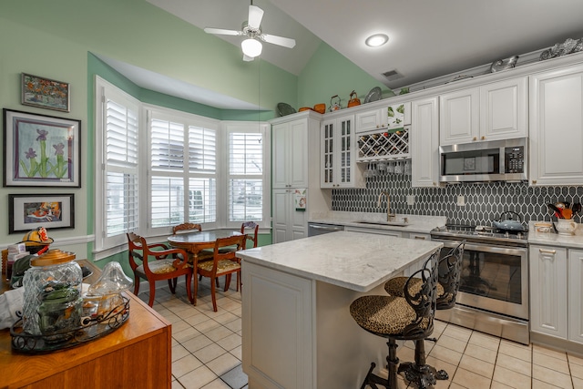 kitchen with stainless steel appliances, sink, ceiling fan, a kitchen island, and white cabinets