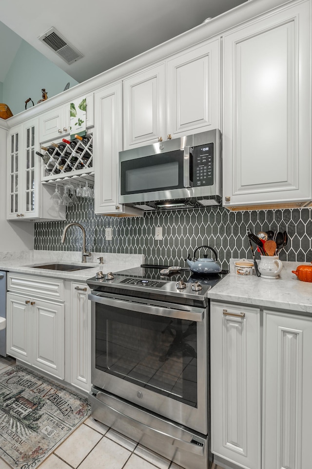 kitchen with stainless steel appliances, sink, light tile patterned floors, backsplash, and white cabinets