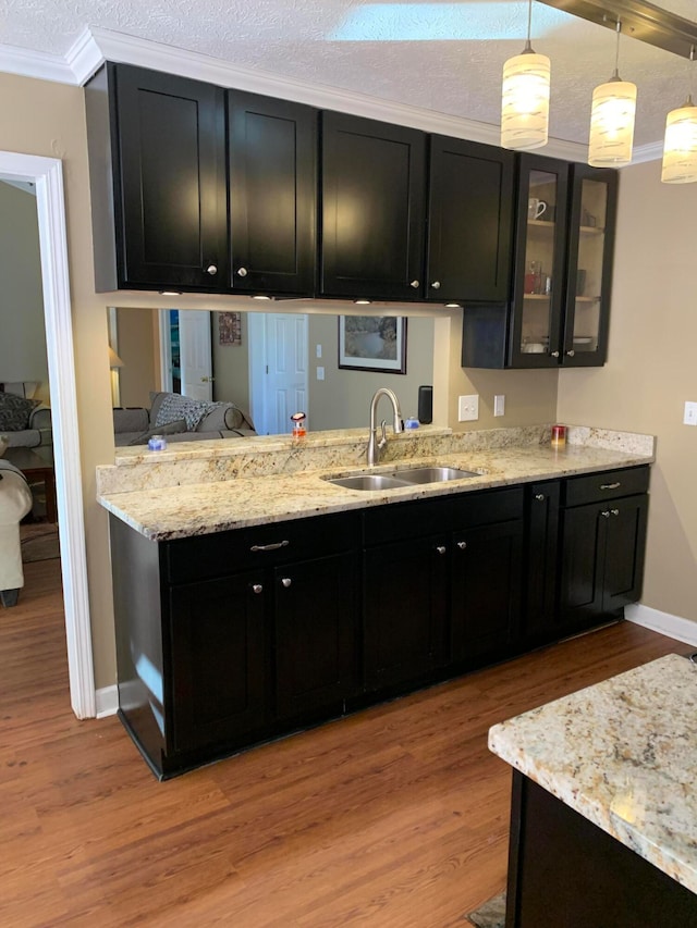 kitchen featuring hanging light fixtures, a textured ceiling, sink, crown molding, and light wood-type flooring