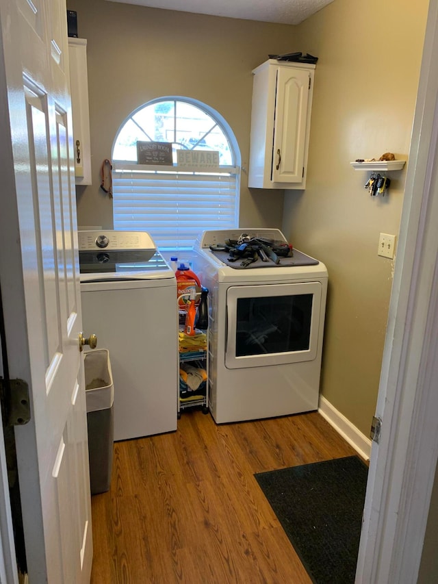 clothes washing area featuring light wood-type flooring, washing machine and dryer, and cabinets