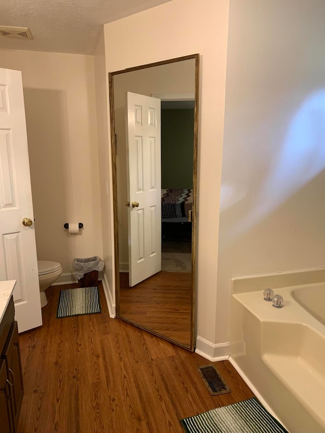 bathroom featuring hardwood / wood-style flooring, a tub to relax in, a textured ceiling, vanity, and toilet