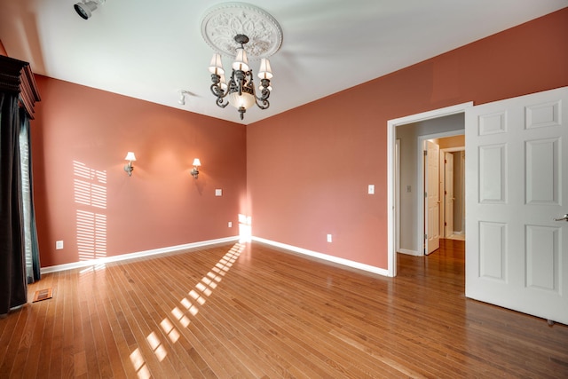 spare room with hardwood / wood-style floors and an inviting chandelier