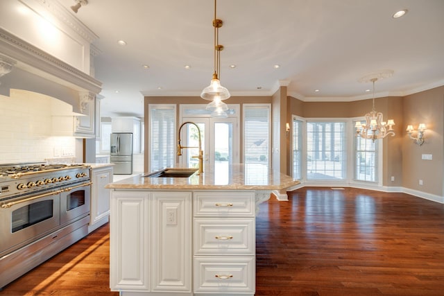 kitchen with stainless steel appliances, sink, white cabinetry, hanging light fixtures, and an island with sink