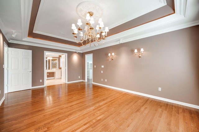 spare room featuring a tray ceiling, an inviting chandelier, light wood-type flooring, and ornamental molding