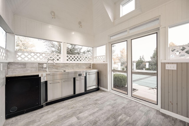 kitchen with a high ceiling, white cabinets, sink, wooden walls, and stainless steel dishwasher