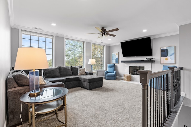 living room featuring ceiling fan, carpet flooring, a brick fireplace, and crown molding