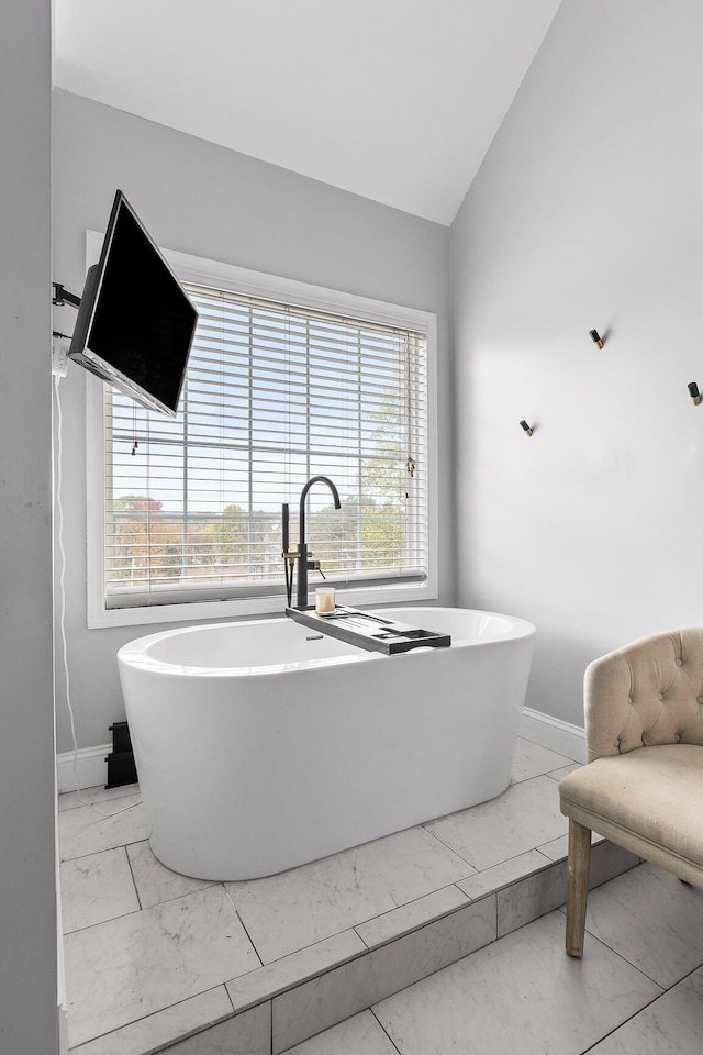 bathroom with a washtub, vaulted ceiling, and plenty of natural light