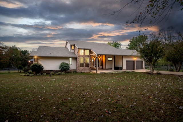 back house at dusk featuring a garage and a yard