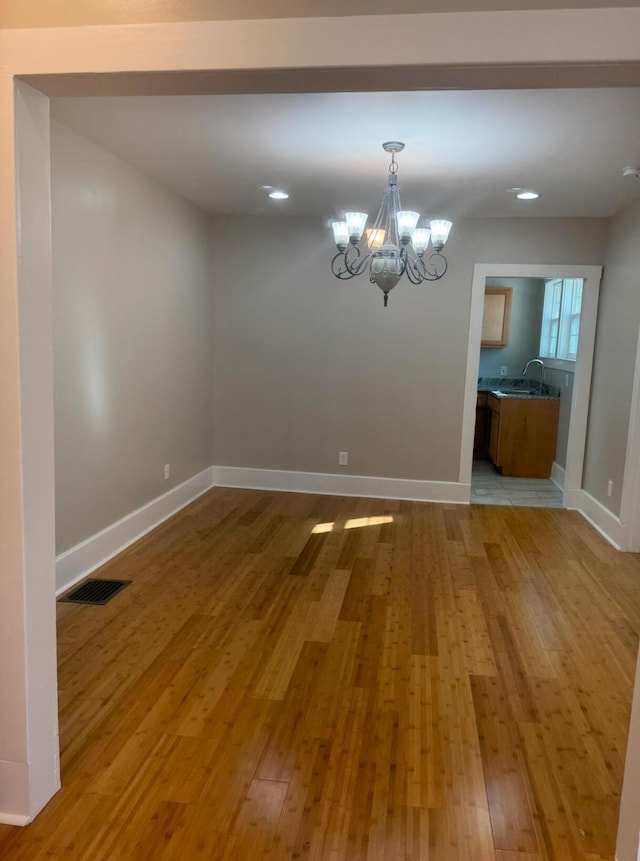 unfurnished dining area featuring sink, light wood-type flooring, and a notable chandelier