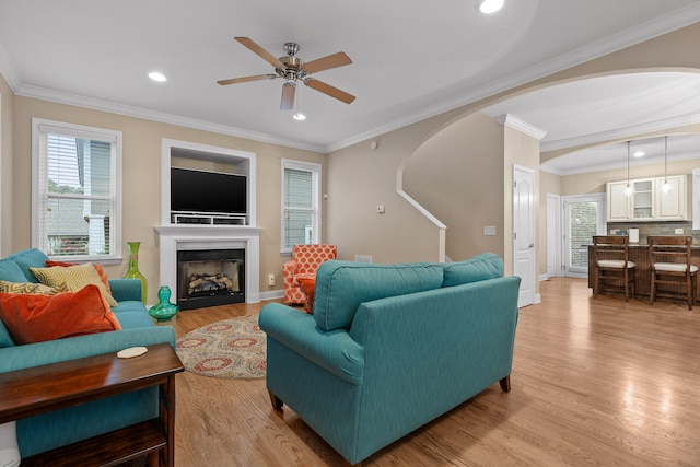 living room with light wood-type flooring, ceiling fan, and crown molding