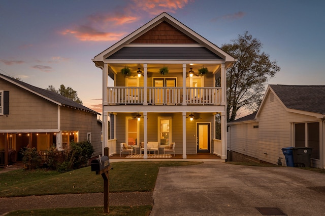 back house at dusk featuring covered porch, a lawn, ceiling fan, and a balcony