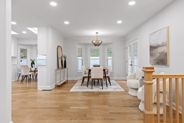 dining room with an inviting chandelier, a healthy amount of sunlight, light wood-type flooring, and french doors