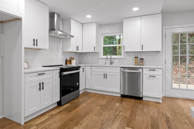 kitchen with dishwasher, black range with electric cooktop, wall chimney exhaust hood, and white cabinetry