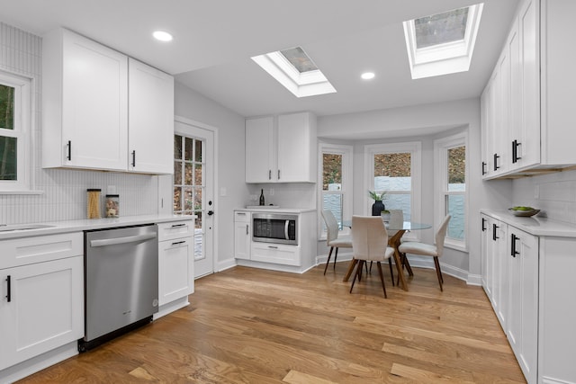 kitchen with white cabinetry, appliances with stainless steel finishes, backsplash, and light hardwood / wood-style flooring