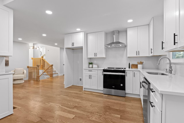 kitchen featuring white cabinets, wall chimney range hood, sink, and appliances with stainless steel finishes