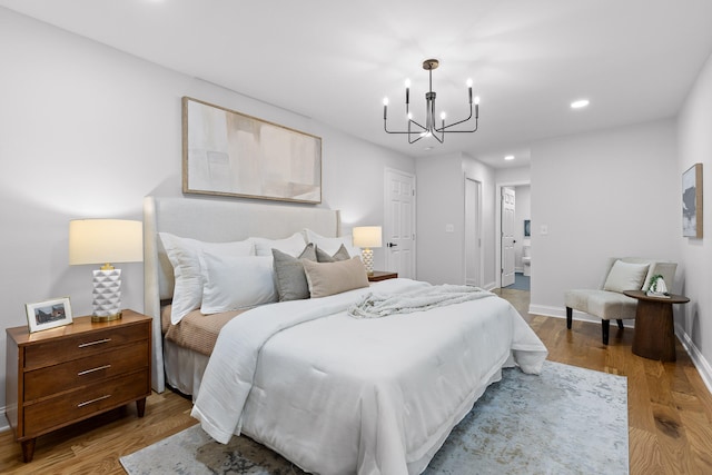 bedroom featuring connected bathroom, light wood-type flooring, and an inviting chandelier