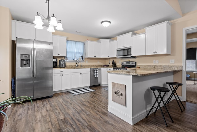 kitchen with kitchen peninsula, appliances with stainless steel finishes, hanging light fixtures, white cabinets, and dark wood-type flooring