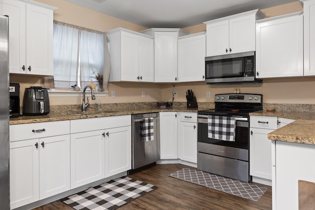 kitchen with dark wood-type flooring, dark stone counters, white cabinets, sink, and appliances with stainless steel finishes