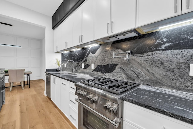 kitchen with tasteful backsplash, dark stone counters, stainless steel stove, light hardwood / wood-style floors, and white cabinets