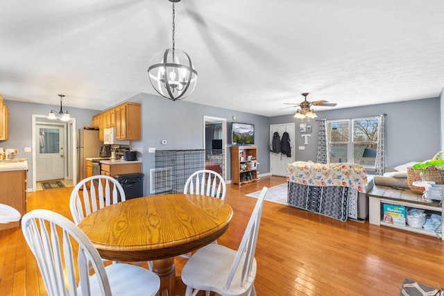 dining space with ceiling fan with notable chandelier and light wood-type flooring