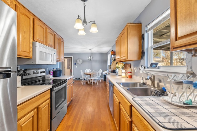 kitchen featuring appliances with stainless steel finishes, decorative light fixtures, sink, a notable chandelier, and light wood-type flooring