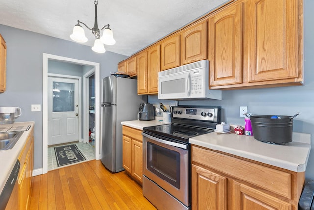 kitchen featuring sink, appliances with stainless steel finishes, hanging light fixtures, a notable chandelier, and light wood-type flooring