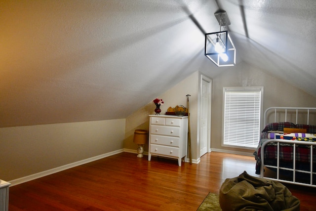 bedroom featuring hardwood / wood-style floors, vaulted ceiling, and a textured ceiling