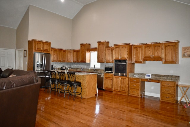 kitchen with a center island, light hardwood / wood-style flooring, high vaulted ceiling, a breakfast bar, and appliances with stainless steel finishes