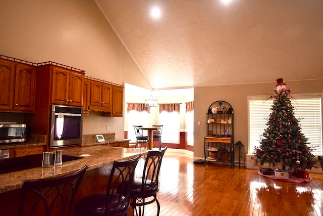 kitchen with stone countertops, appliances with stainless steel finishes, a textured ceiling, high vaulted ceiling, and dark hardwood / wood-style flooring