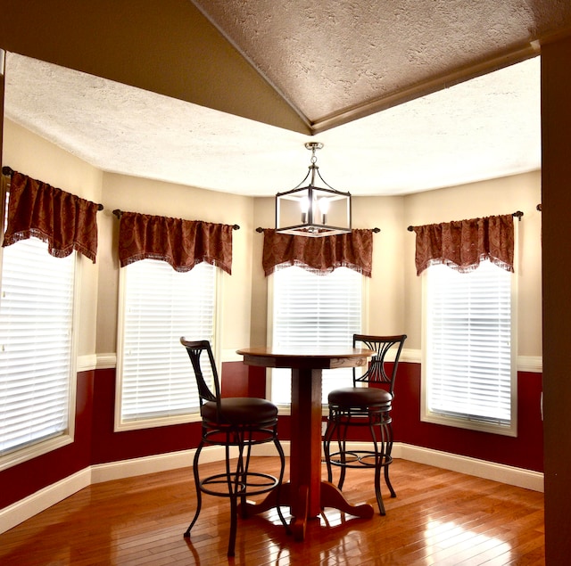 dining area with hardwood / wood-style floors, lofted ceiling, a textured ceiling, and an inviting chandelier