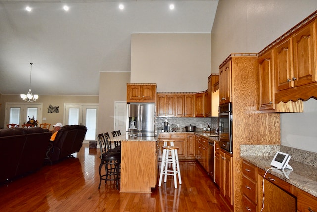 kitchen with a kitchen bar, stainless steel appliances, dark wood-type flooring, a center island, and light stone countertops