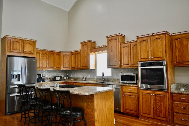 kitchen with dark hardwood / wood-style flooring, a center island, sink, a breakfast bar, and appliances with stainless steel finishes