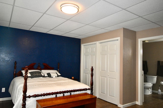 bedroom with ensuite bathroom, a paneled ceiling, and dark tile patterned flooring