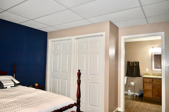 tiled bedroom with ensuite bath, a paneled ceiling, sink, and multiple closets