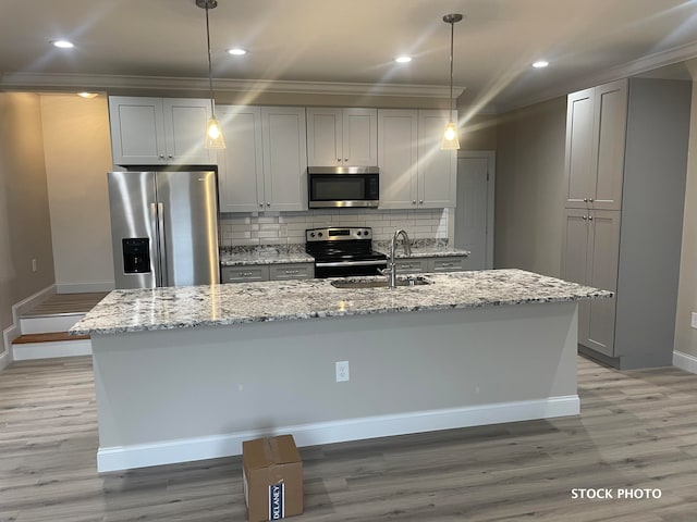 kitchen featuring appliances with stainless steel finishes, sink, light stone counters, and a kitchen island with sink