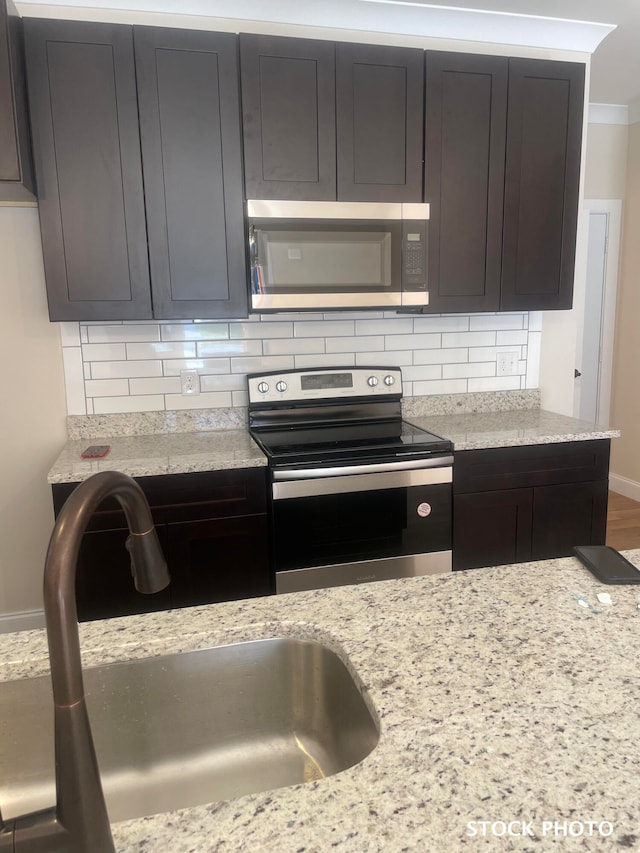 kitchen with hardwood / wood-style flooring, sink, tasteful backsplash, light stone countertops, and appliances with stainless steel finishes