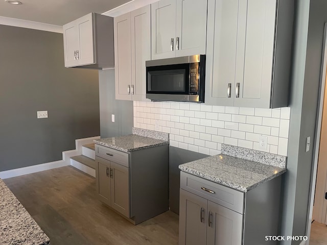 kitchen featuring tasteful backsplash, ornamental molding, gray cabinets, dark hardwood / wood-style floors, and light stone countertops