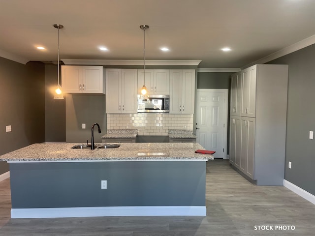 kitchen featuring pendant lighting, a kitchen island with sink, and light stone countertops