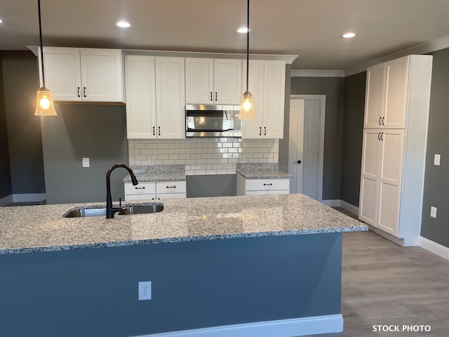 kitchen with white cabinets, hanging light fixtures, sink, light stone countertops, and light wood-type flooring