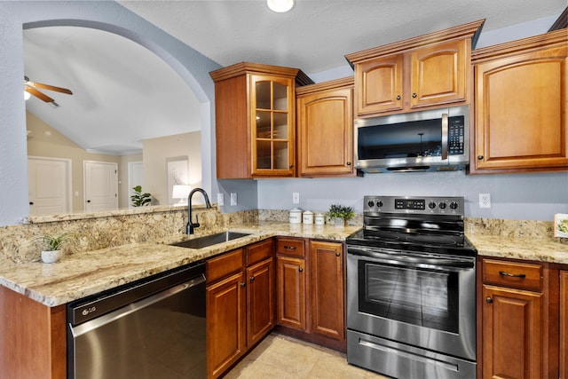 kitchen featuring lofted ceiling, sink, appliances with stainless steel finishes, ceiling fan, and light stone countertops