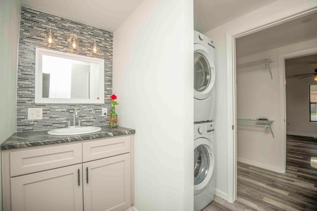 laundry room featuring ceiling fan, stacked washer and dryer, wood-type flooring, and sink