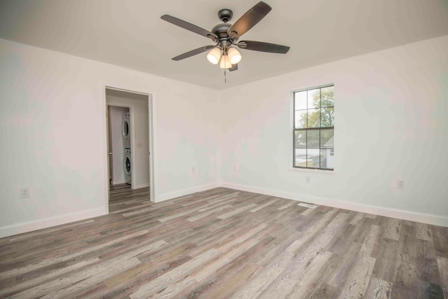 spare room featuring stacked washer / dryer, hardwood / wood-style floors, and ceiling fan