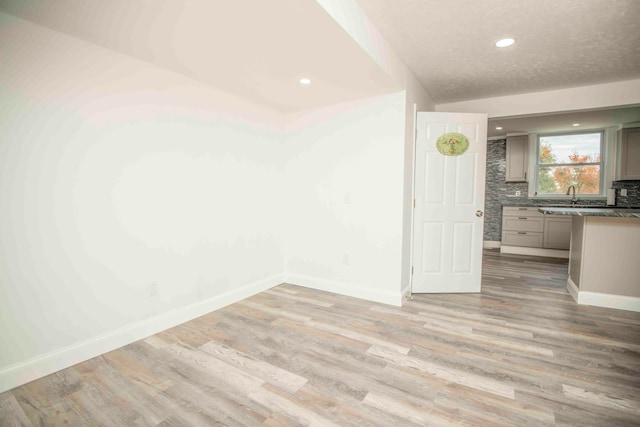 spare room with a textured ceiling, light hardwood / wood-style floors, lofted ceiling, and sink