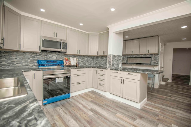 kitchen featuring stainless steel appliances, light hardwood / wood-style floors, kitchen peninsula, gray cabinets, and decorative backsplash