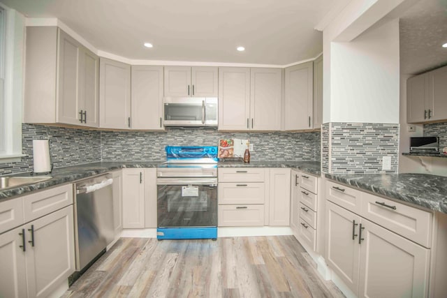 kitchen with decorative backsplash, appliances with stainless steel finishes, light hardwood / wood-style floors, and dark stone countertops