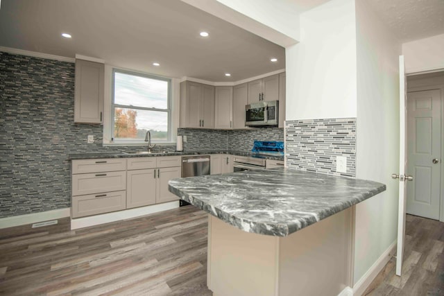 kitchen with kitchen peninsula, stainless steel appliances, hardwood / wood-style floors, and tasteful backsplash