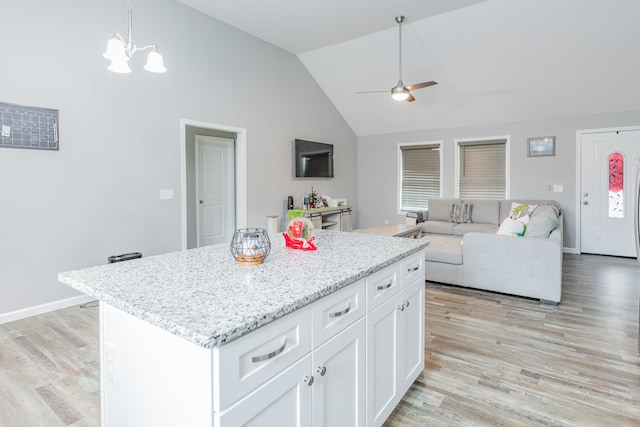 kitchen with ceiling fan with notable chandelier, white cabinets, hanging light fixtures, a kitchen island, and light wood-type flooring