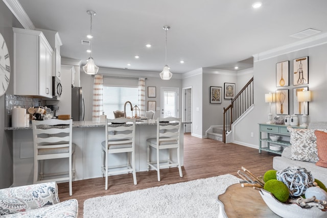 kitchen with ornamental molding, white cabinetry, appliances with stainless steel finishes, a kitchen bar, and hanging light fixtures