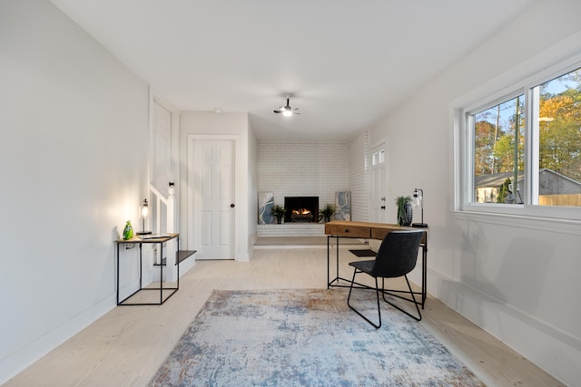 office space with ceiling fan, light hardwood / wood-style floors, and a brick fireplace