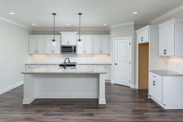 kitchen featuring light stone counters, a kitchen island with sink, white cabinets, pendant lighting, and dark hardwood / wood-style flooring